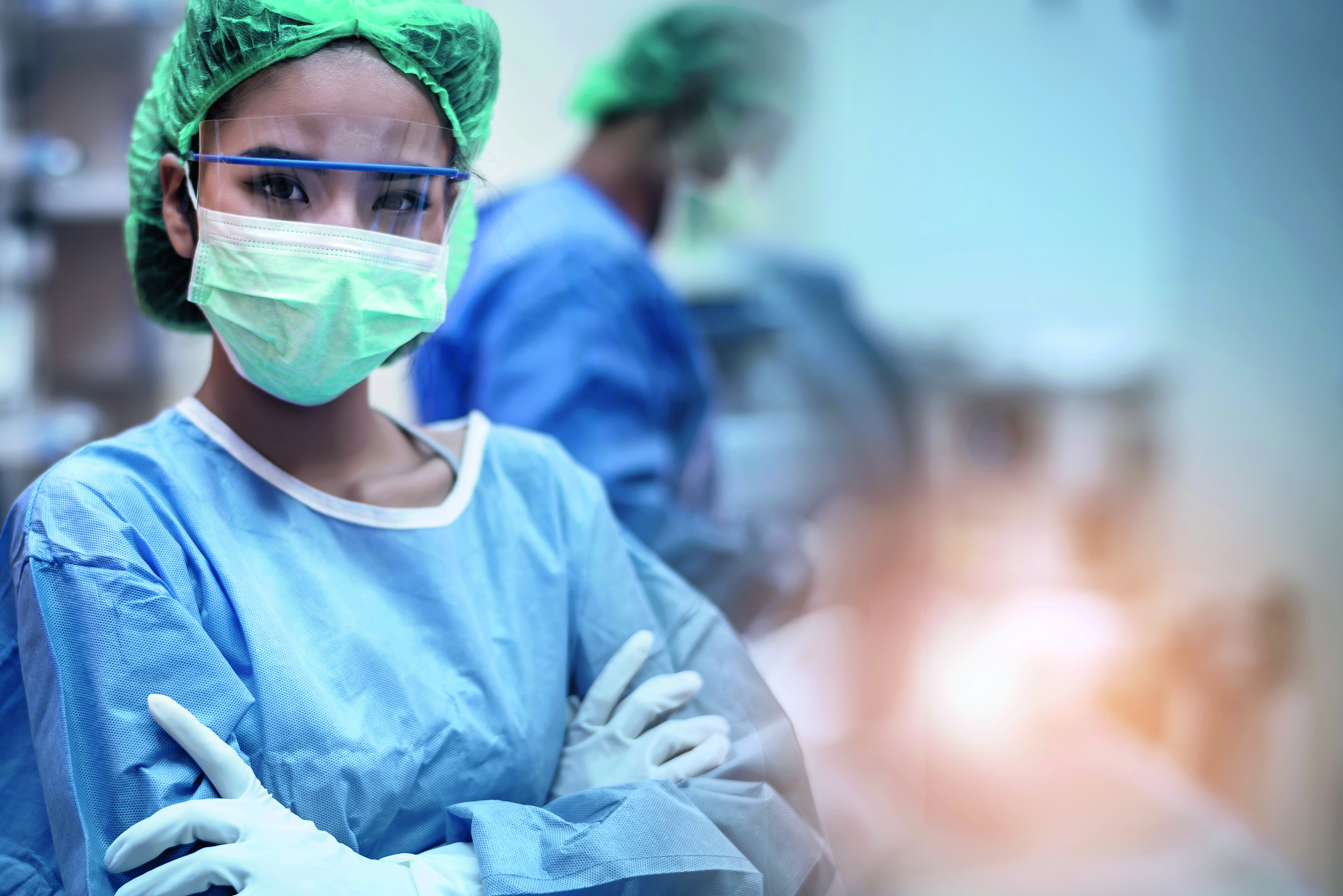 Surgeon wearing scrubs in operating theatre with other surgeons in the background performing an operation using surgical instruments
