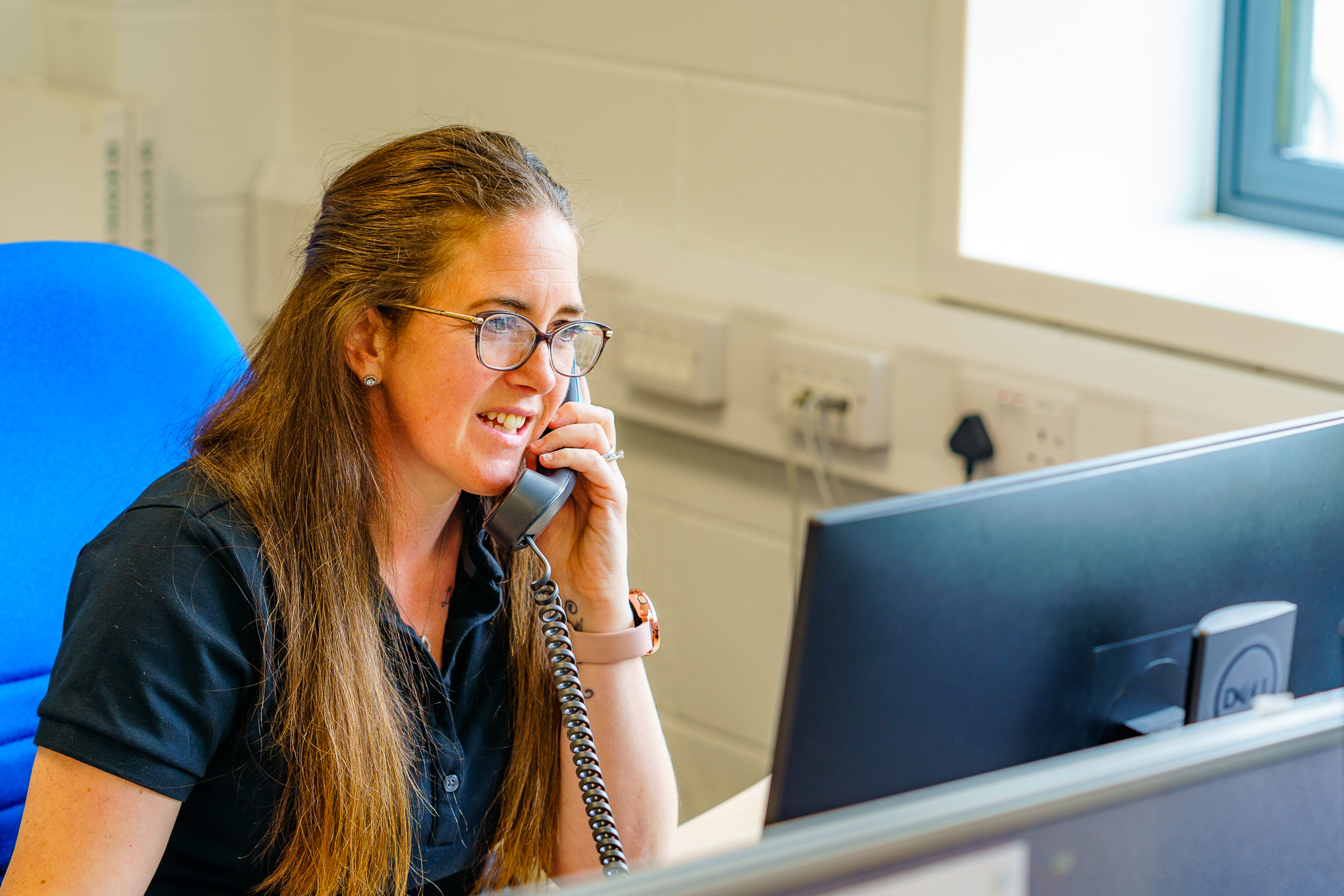 Customer relations coordinator answering a phone call at her desk in the office.