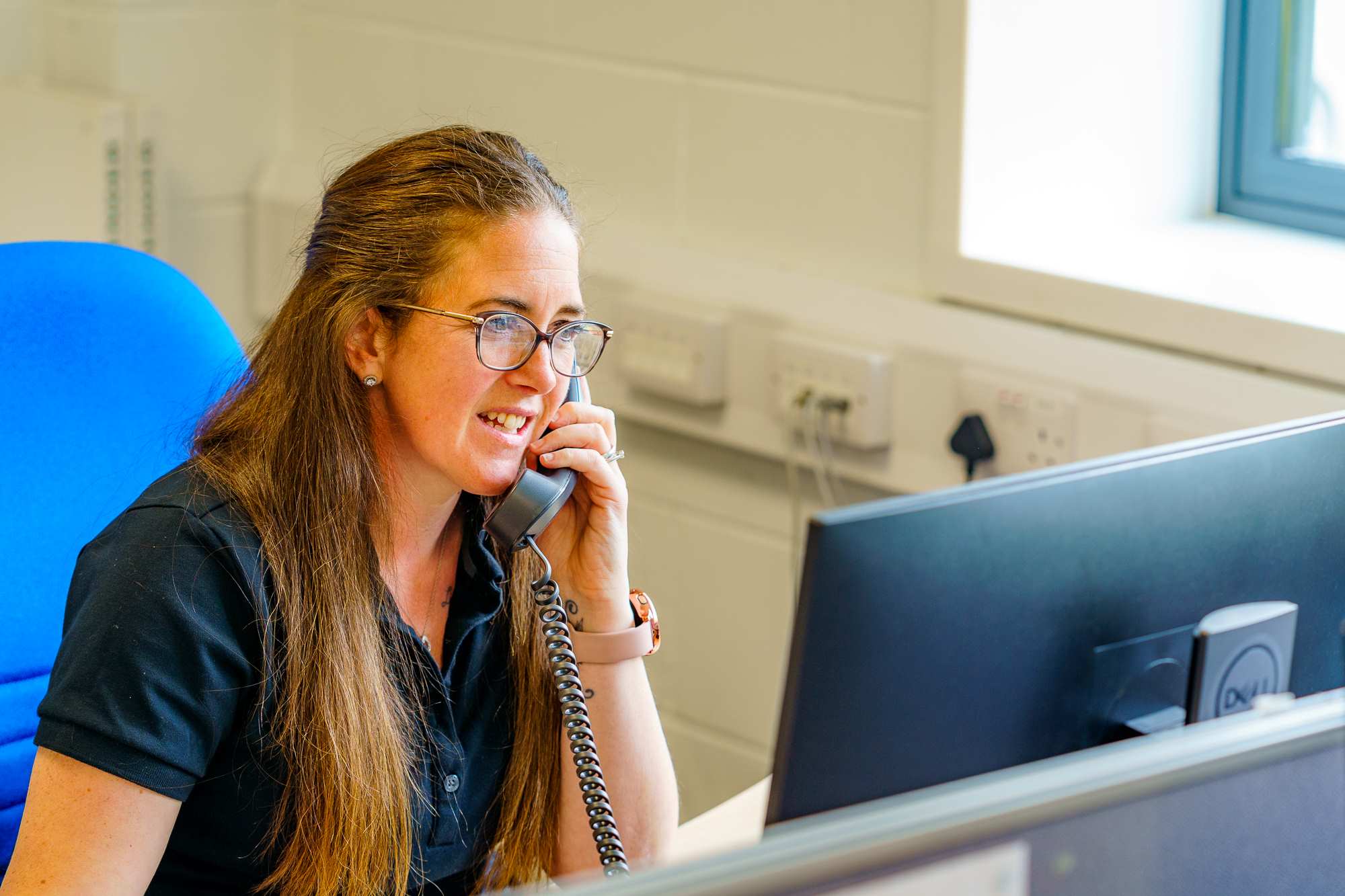 Customer relations coordinator answering a phone call at her desk in the office.