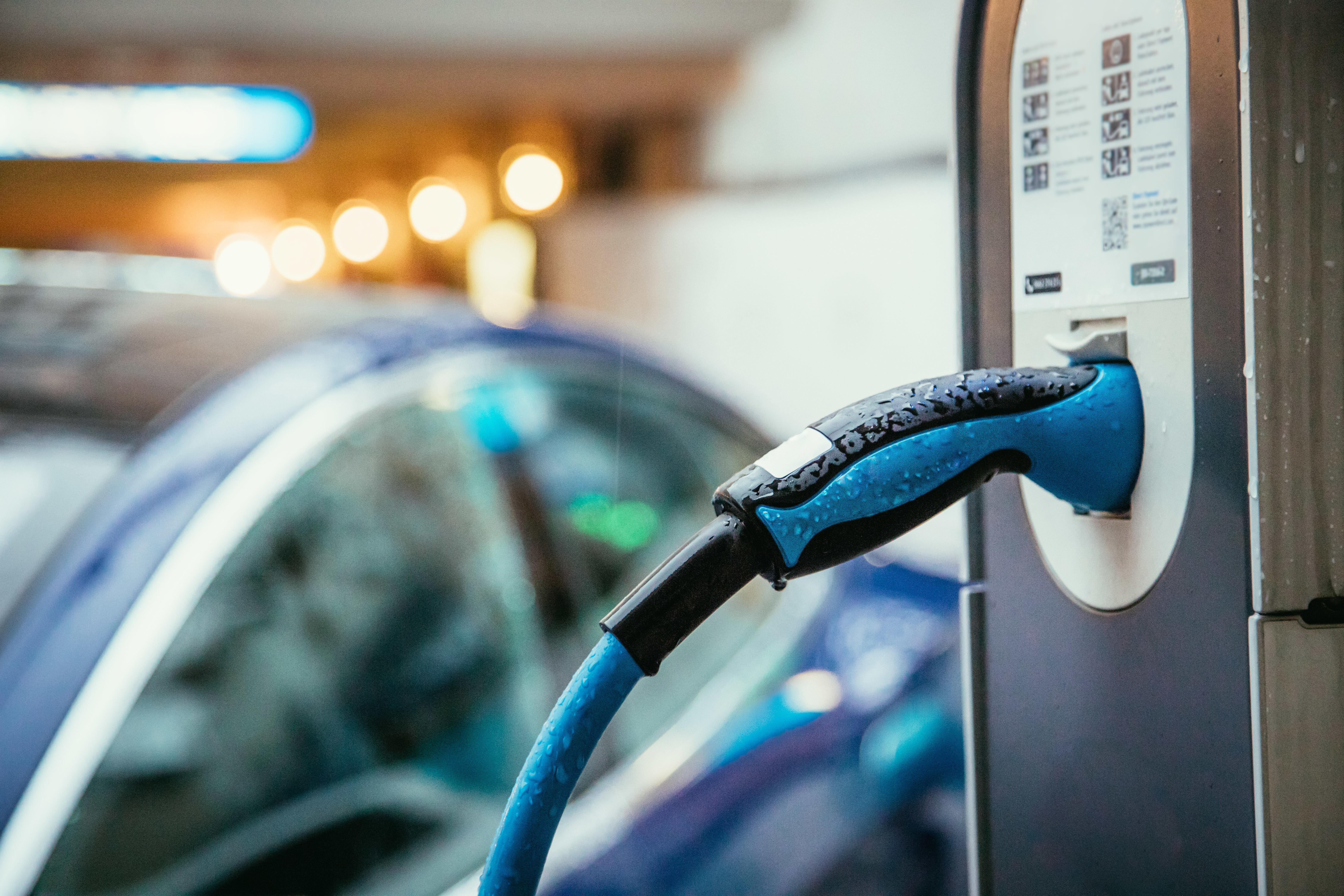 An electric vehicle (EV) charging with a charging cable plugged into the car, with the charging station visible in the foreground