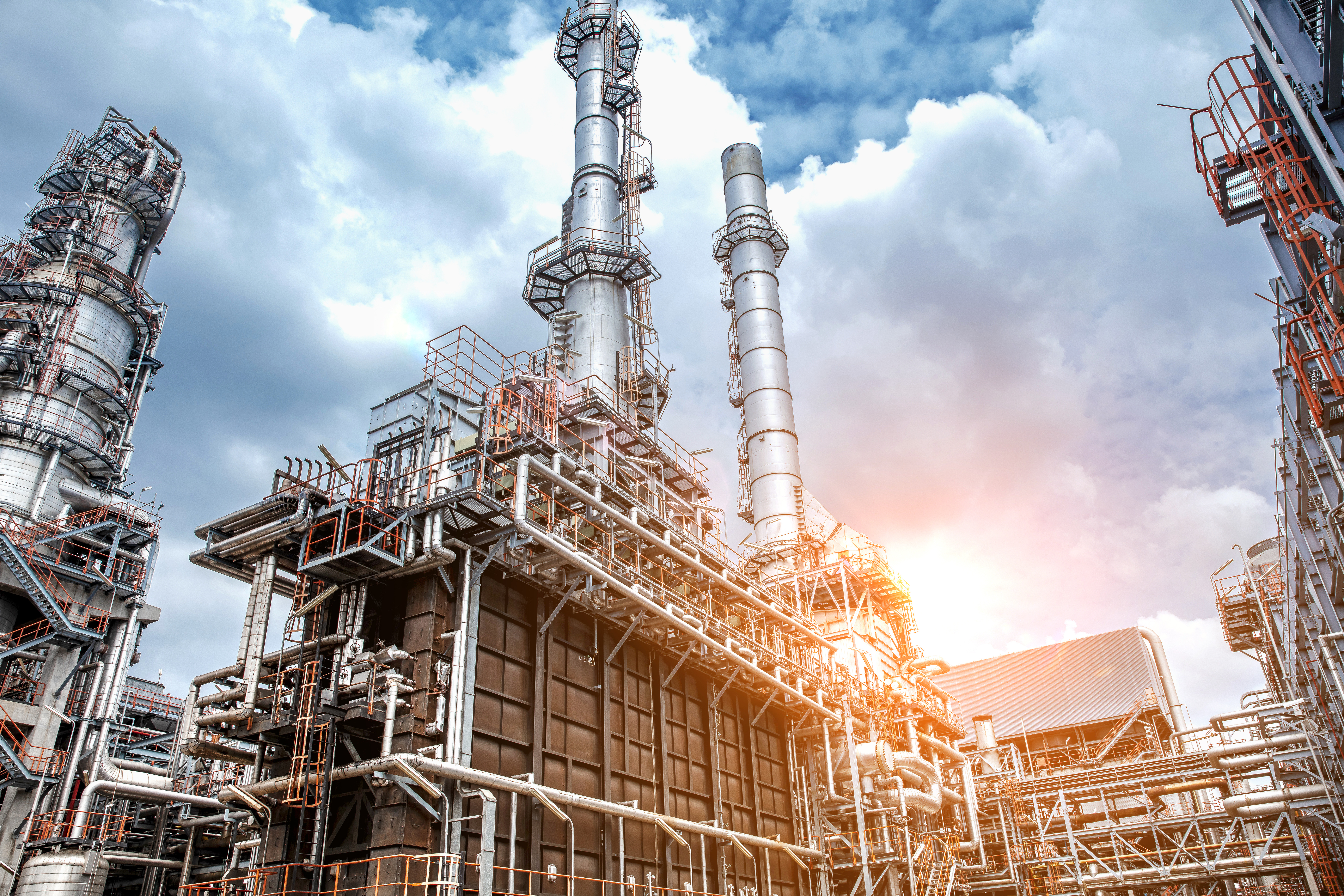 An industrial oil refinery with large tanks, pipes, and smokestacks showcasing the complex machinery and infrastructure involved in the refining process.