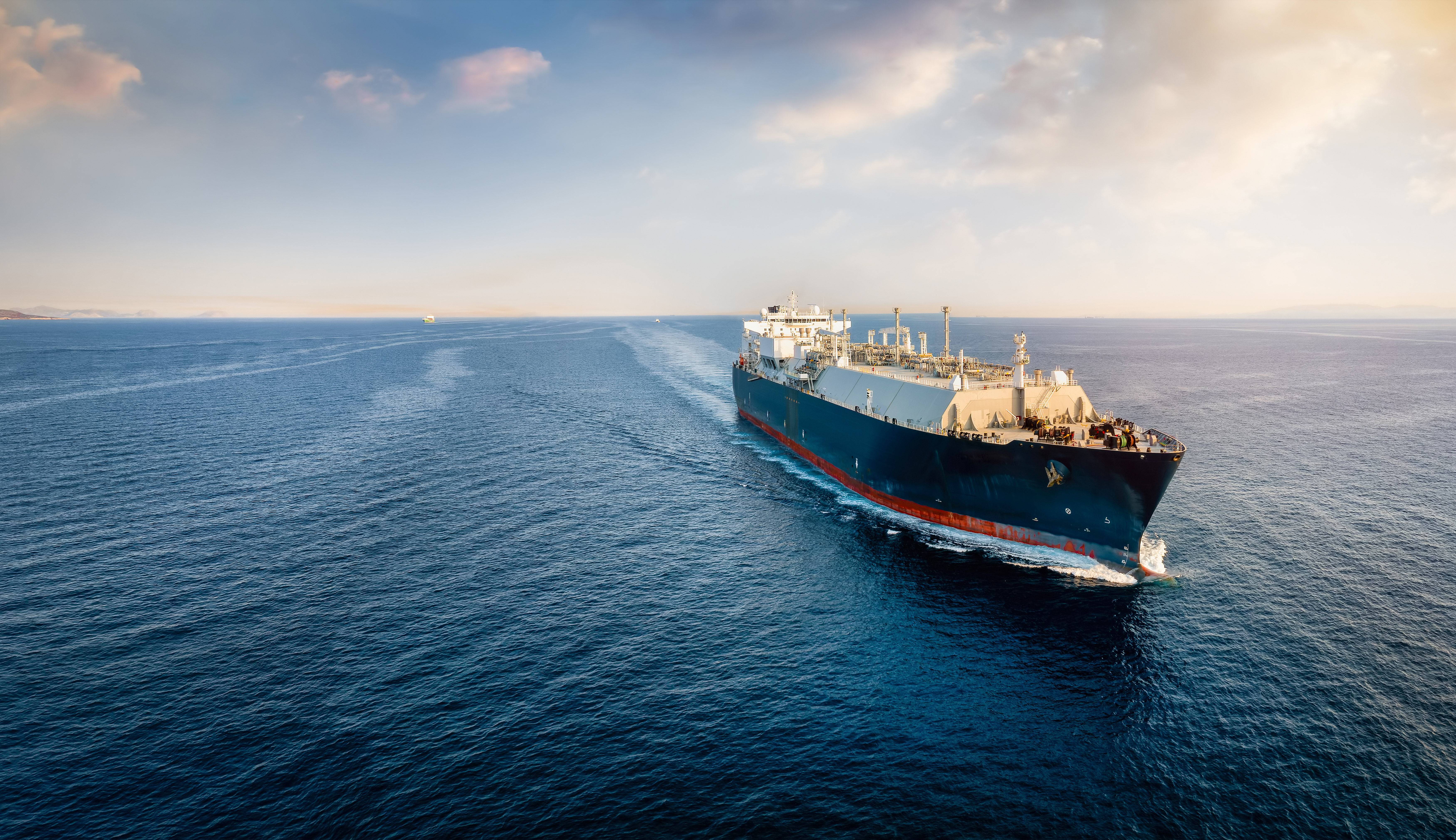 A large ship sailing on open water, with the vast ocean stretching out to the horizon under a clear sky.