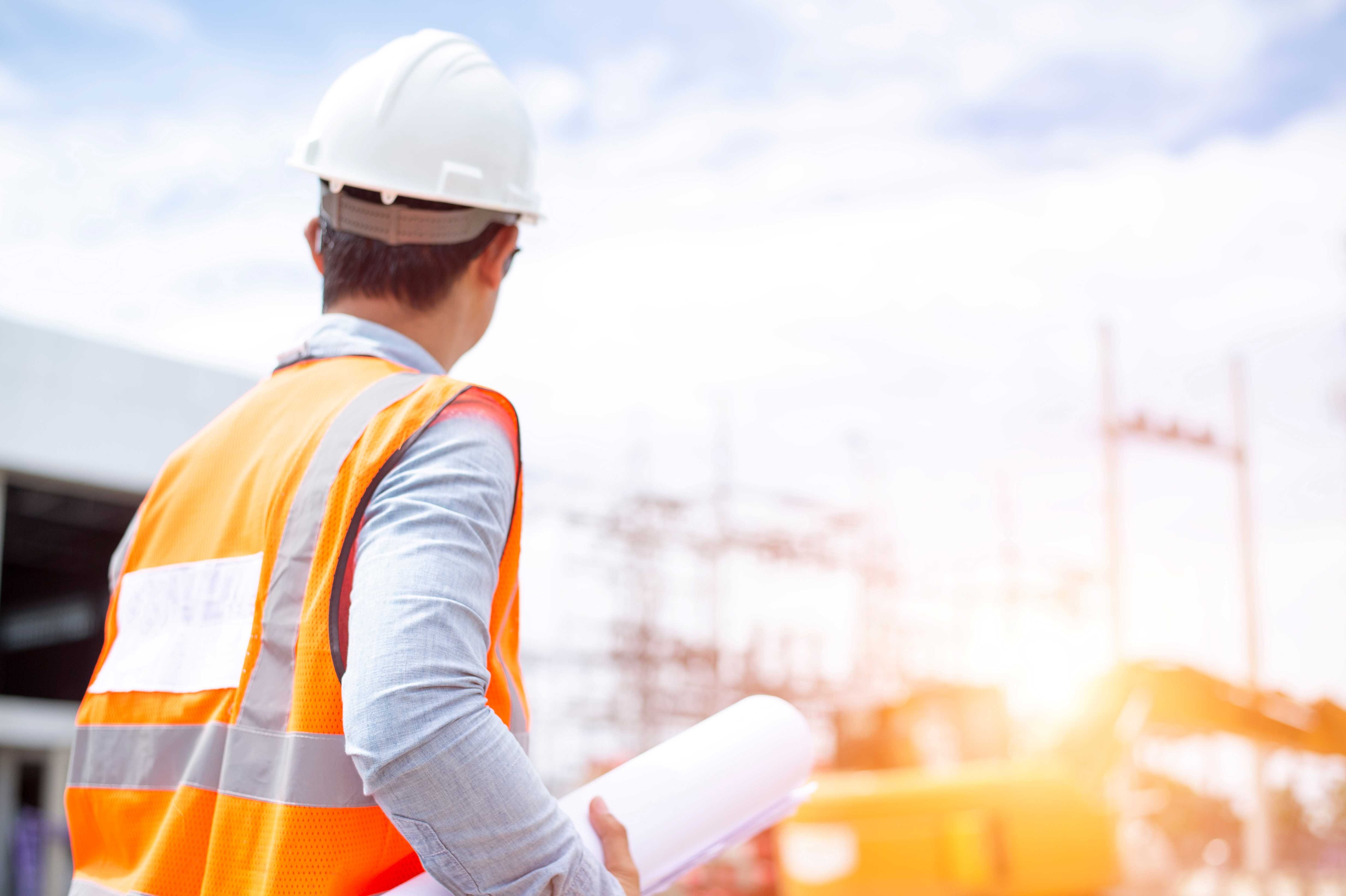 Image of an engineer stood in front of building infrastructure with a drawing in hand