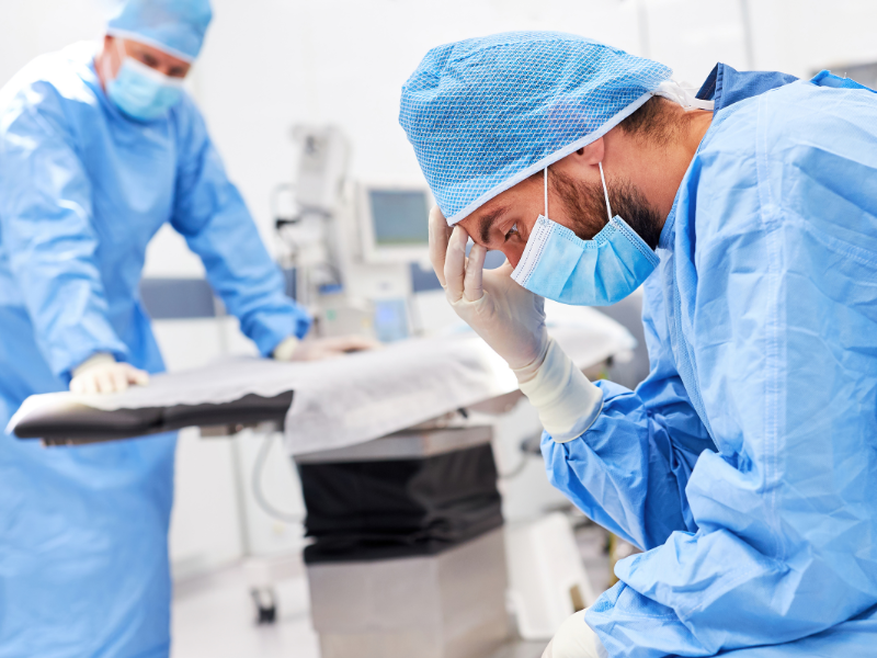 Silver and black operating table with two surgeons looking frustrated, both wearing blue hospital gowns  