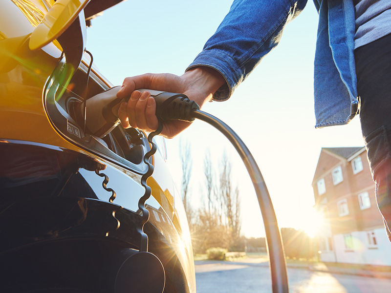 Image of a person's arm putting an electric vehicle charger in their vehicle to charge their car